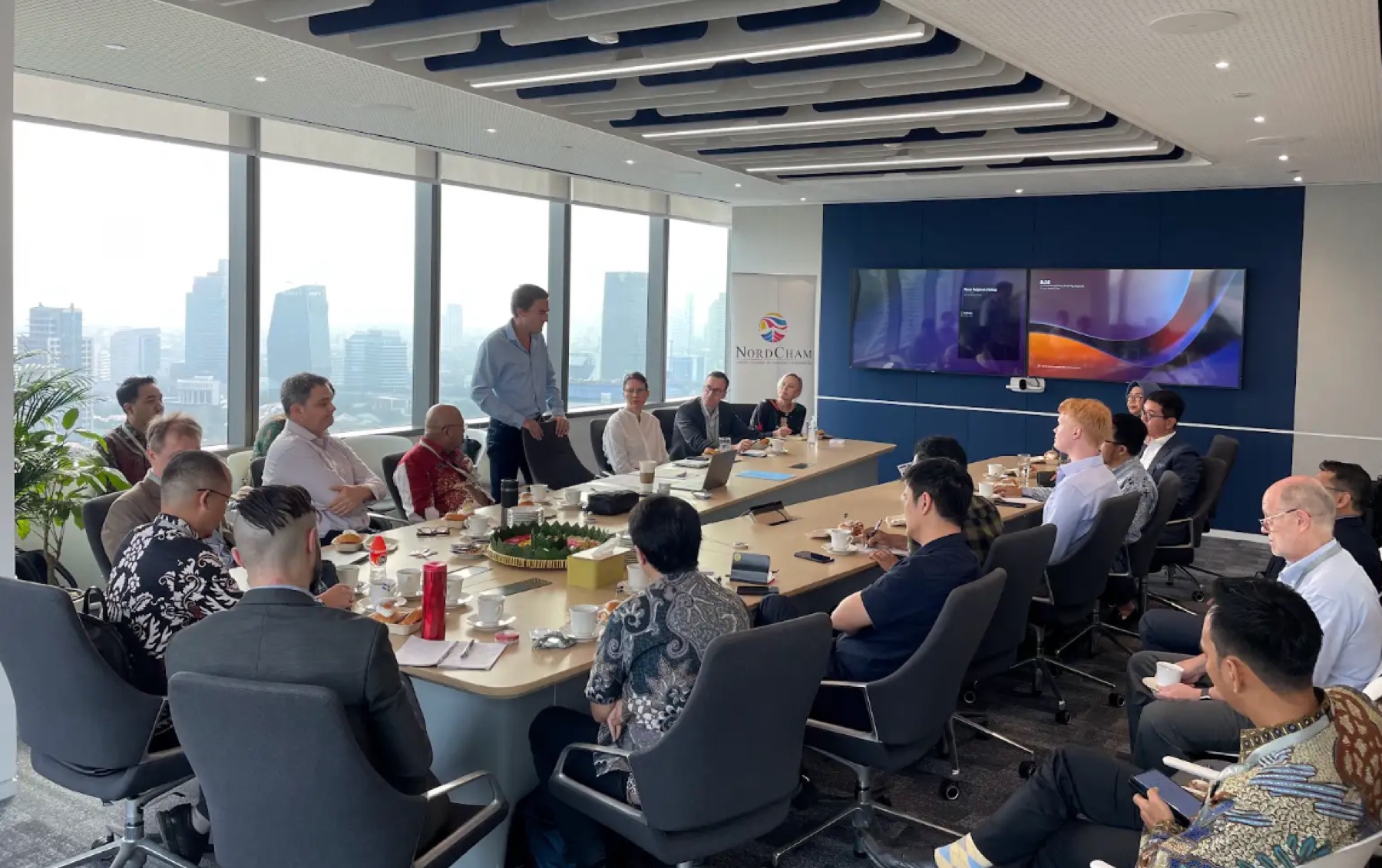 A roundtable high above Jakarta, a NordCham roll-up banner beside the screen