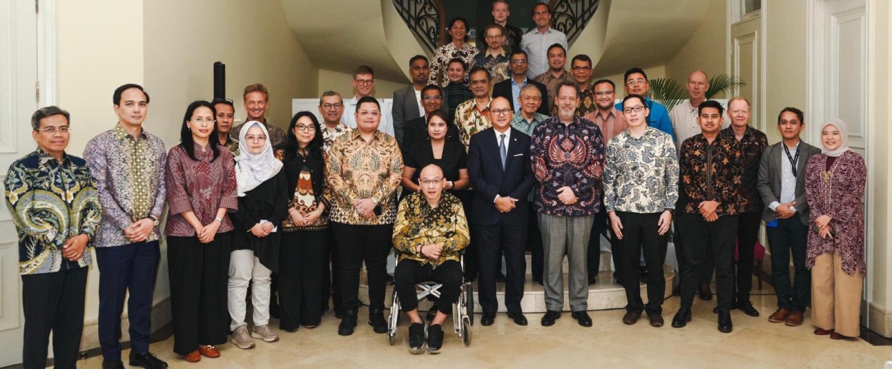 A large group standing for a photograph on a staircase, many in batik