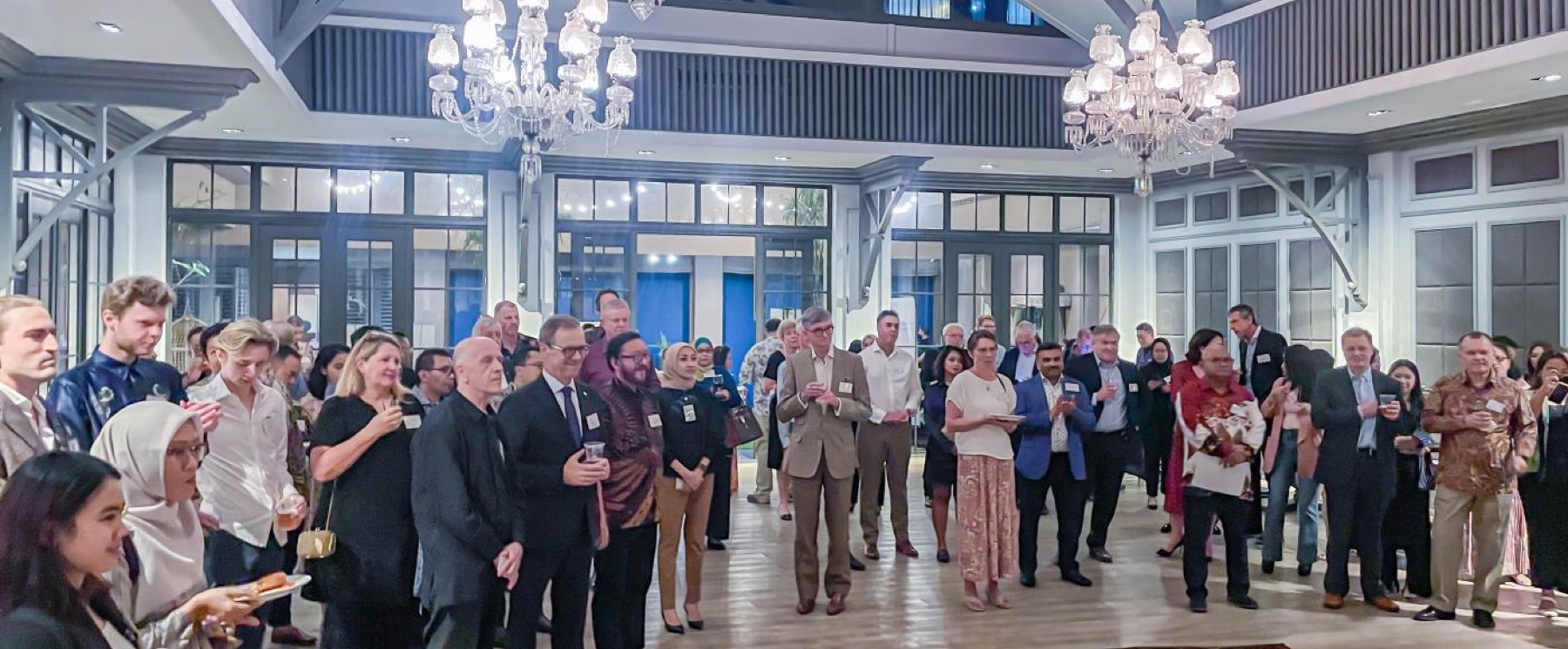 A crowded reception under chandeliers, guests with name badges and glasses